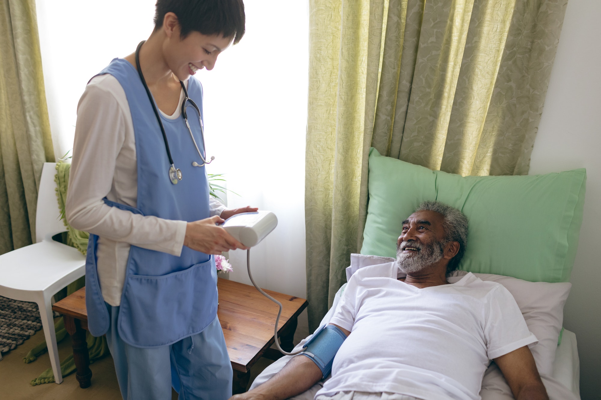 Asian female nurse checking blood pressure of African-american senior male patient